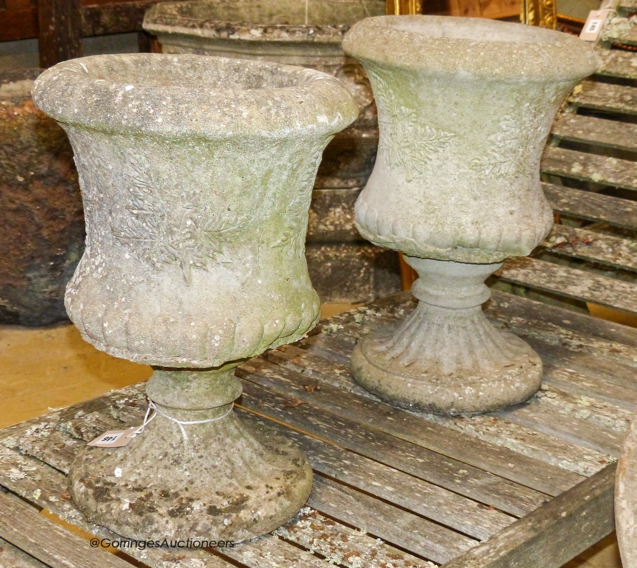 A pair of reconstituted stone campana-shaped urns on stands, decorated with ferns, diameter 34cm, height 49cm